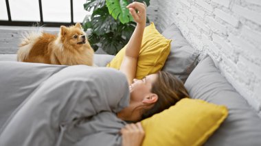 Güzel, genç, İspanyol bir kadın rahatlatıcı bir sabah geçiriyor, evcil köpeğiyle rahat bir yatakta uyuyor, mutlu bir gülümsemeyle huzurlu bir şekilde yatak odasında uyanıyor.