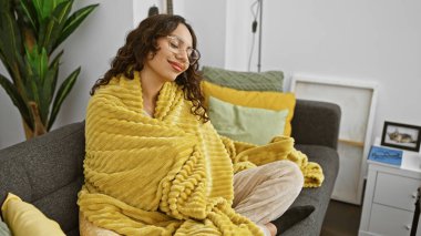 Memnun bir kadın, rahat, şık bir oturma odasında sarı bir battaniyeyle kanepede dinlenir..