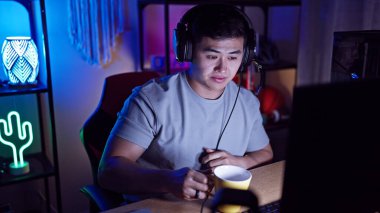 Oyun odasında kulaklıklı Asyalı genç bir adam. Geceleri neon ışıklarla aydınlatılıyor..