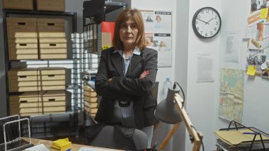 Kendine güvenen orta yaşlı kadın dedektif kollarını kavuşturmuş, saat, dosyalar ve tahtalarla soruşturmayı ima ediyor..