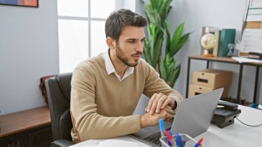 Modern ofis ortamında dizüstü bilgisayarla çalışan sakallı yakışıklı bir İspanyol..