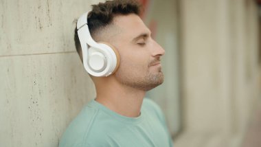 Young hispanic man listening to music standing at street