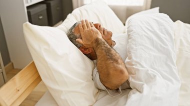 Olgun, gri saçlı bir adam yatakta yatarken stresi ya da uykusuzluğu temsil eder..