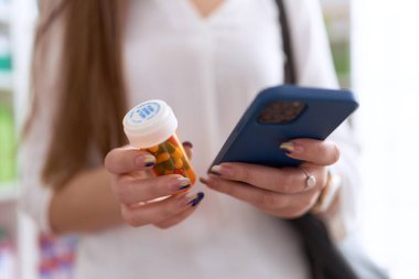 Genç ve güzel bayan müşteri eczanede akıllı telefon kullanıyor.