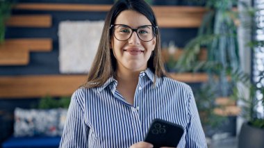 Ofiste akıllı telefon kullanarak mutlu gülümseyen güzel İspanyol kadın.