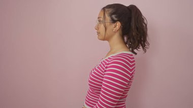 Gözlüklü genç bir İspanyol kadının profili pembe izole edilmiş bir arka planda, düşünceli ve düşünceli bir ifadeyi canlandırıyor..