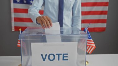 Arka planda Amerikan bayrağı olan, demokrasi ve vatandaşlığı somutlaştıran bir seçim merkezinde oy kullanan bir adam..
