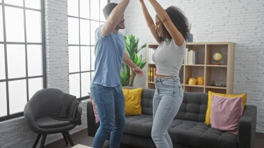 Neşeli bir erkek ve kadın modern bir oturma odasında neşeyle dans ediyor, gündelik bir evde sevgi ve mutluluk sergiliyorlar..