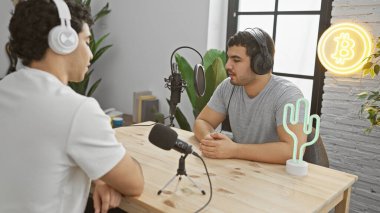 İki adam, modern bir stüdyoda, neon ışıklı bir bitcoin ile podcast sohbeti yaptılar.
