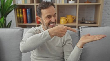 Sakallı, orta yaşlı, gülümseyen ve rahat bir oturma odasında sunum yapan bir adam.