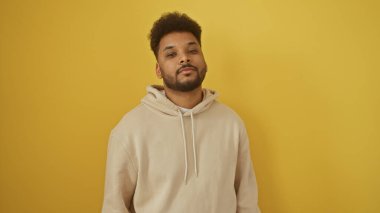 Afro-amerikan bir adam günlük kıyafetiyle canlı sarı bir arka plana karşı güvenle poz veriyor.