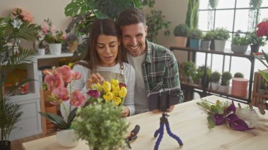 Çiçek düzenleyen bir kadın ve bir erkek çiçekçi dükkanında özel ders çekiyorlar..