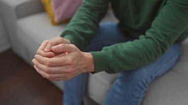 Bir adamın kapalı bir koltukta otururken sıkıca sarılmış ellerini, bir ev ortamında rahatlama ya da tefekkür tasvir ederken..