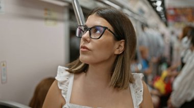 Güzel İspanyol kadın, gözlüklü, metro geçişinde bekliyor, şehir şehrinin boş yeraltı demiryolundaki modern esmer yolcu portresi, toplu taşıma araçlarıyla seyahat ediyor.