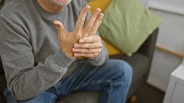 Rahat bir evde bileği ağrıyan gri saçlı bir adam..