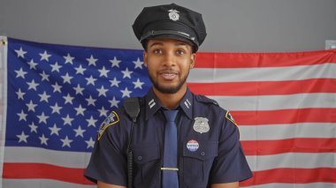 Kendine güvenen bir Afro-Amerikan polisi profesyonel bir ortamda Amerikan bayrağının önünde duruyor..