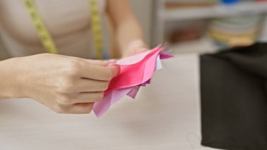 Modern bir atölyede terzilik ve moda tasarımını temsil eden kumaş örneklerini tutan bir kadının ellerinin yakın çekimi..