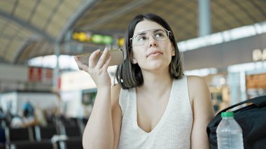 Havaalanında sesli mesaj dinleyen genç, güzel bir İspanyol kadın.