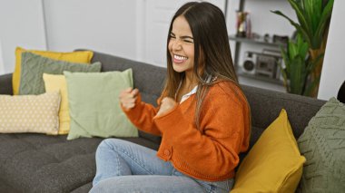 Neşeli, genç, İspanyol bir kadın renkli yastıklarla sıcak bir oturma odasında kutlama yapıyor..