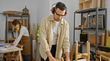 Bir erkek ve bir kadın marangoz takımı iyi donanımlı bir marangoz atölyesinde birlikte çalışarak mobilya yapımına odaklanıyor..