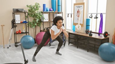 Afrika kökenli Amerikalı bir kadın spor salonunda spor aletleriyle çömelme egzersizi yapıyor..