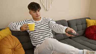 Çekici, genç İspanyol bir adamın rahatlatıcı yaşam tarzı, TV 'de film izlemesi, elinde kahve fincanı, oturma odasındaki kanepede dinlenmesi.