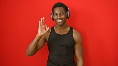 Gülümseyen Afrikalı Amerikalı adam kırmızı arka planda kulaklık takıyor.