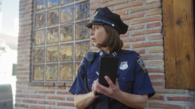 Odaklanmış bir kadın polis memurunun, dışarıdaki bir not defterine tuğladan bir duvara not yazışının yan görüntüsü..