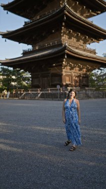 Güzel İspanyol kadın ayakta, güvenle gülümsüyor Japonya 'nın To-ji tapınağının önünde, mutluluk ve kaygısız neşe saçıyor, dostça ifadesi bu Kyoto parkını daha da eğlenceli hale getiriyor..