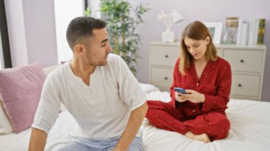 Pijamalı bir çift yatak odasında dinleniyor, telefonuna sarılmış bir kadın ve ona bakan bir adam..