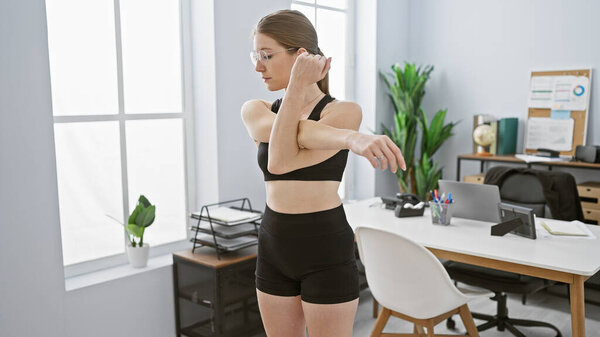 A young woman stretches in a modern office setting, showcasing wellbeing at the workplace.