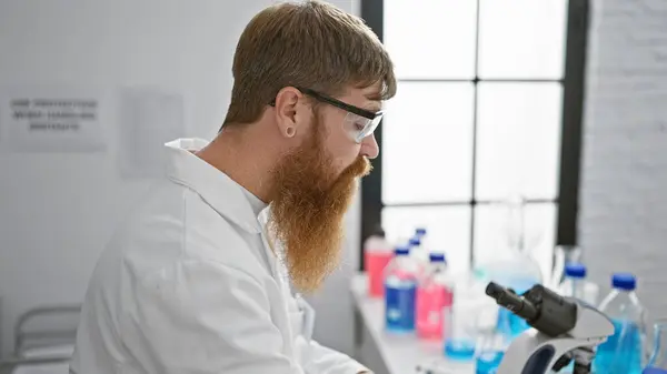 Relaxed yet serious-faced, young redhead male scientist, amped about a groundbreaking experiment in the lab, ensures safety with security glasses