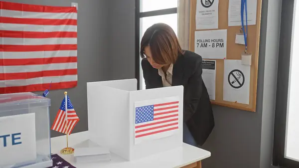 stock image A professional african american woman voting indoors at a us electoral polling station with an american flag in the background.