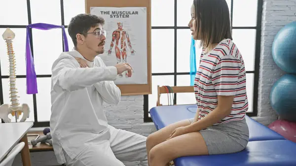 stock image A man physiotherapist in a clinic guides a woman patient during rehab, with exercise equipment visible.