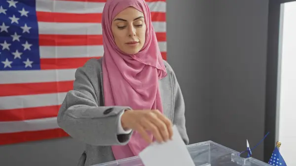 ヒジャーブを着た若い女性がアメリカの国旗を背景に選挙カレッジで投票します — ストック写真