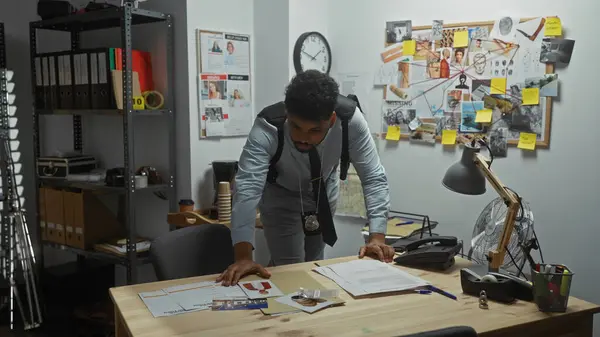 stock image African american detective analyzes evidence in a police office with a board covered in case photos and notes.