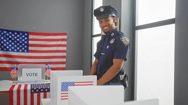 stock image African american policeman smiling in a voting center with us flags.