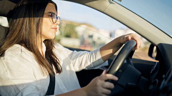 Молодая красивая латиноамериканка за рулем машины, улыбающаяся в очках на дороге