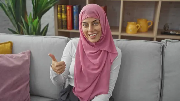 Lächelnde Frau Hijab Gibt Drinnen Auf Gemütlichem Wohnzimmersofa Daumen Hoch Stockbild