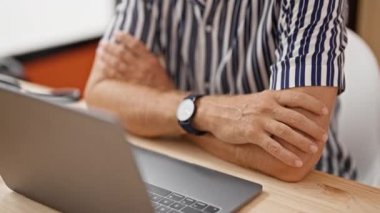 Kollarını çapraz bağlamış, gözlüklü ve çizgili gömlekli kendinden emin bir adam ofisinde çalışıyor..