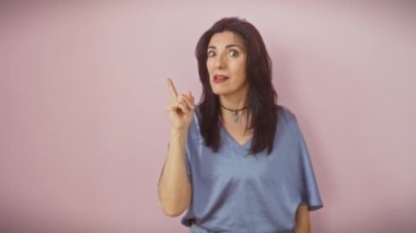 Heyecanlı orta yaşlı İspanyol kadın, ayakta, sevinçle bir parmağını kaldırıyor. Parlak fikir yüzünü aydınlatıyor, başarısını sergiliyor, pembe izole bir arka planda.