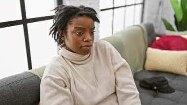 Rasta bukleli neşeli siyah kadın, oturma odasındaki kanepede rahat rahat oturuyor. Başarılı 