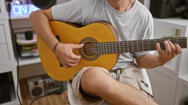 Sakallı bir adam modern bir stüdyo ortamında neşeyle akustik gitar çalar..