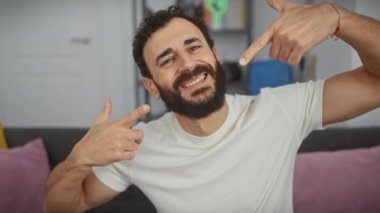 Neşeli orta yaşlı bir adam evde mükemmel dişler sergiliyor, beyaz tişört giyip ağza işaret ediyor - diş sağlığı için kafa sallıyor.