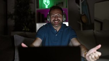 Kulaklıklı orta yaşlı bir adam geceleri rahat bir oturma odasında başarıya işaret eder.