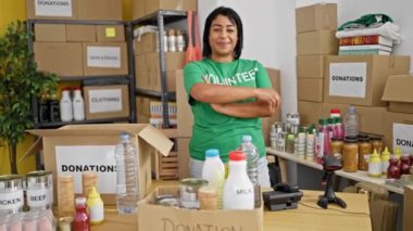Gülümseyen bir kadın bağış merkezinde kutular, yiyecekler ve kıyafetlerle duruyor..