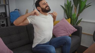 Yakışıklı orta yaşlı bir adam, mutlu, rüya gibi bir gülüşü var, beyaz bir tişörtle evde poz veriyor, elleri üzerinde uyuyor, yorgun ama pozitif..