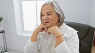 Gri saçlı son sınıf öğrencisinin portresi. Düşünceli bir şekilde parlak bir ofis odasında oturuyor. Tecrübe ve bilgelik yayıyor..