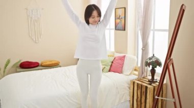 Genç Asyalı bir kadın neşeyle uzanır. Parlak, rahat bir yatak odasında. Yatak, makrome ve sanat eserleriyle..