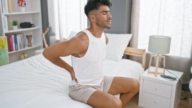 Genç İspanyol bir adam acı içinde, bir yatak odasında otururken sırtına dokunuyor, sağlık ve yaşam tarzını betimliyor..